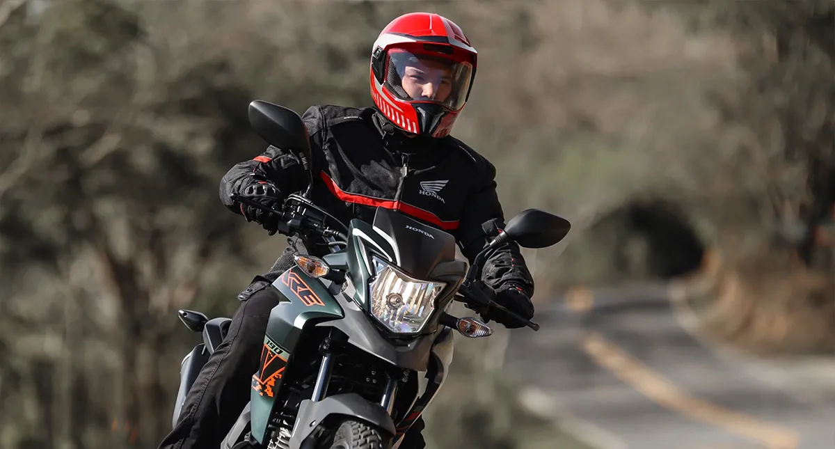 Piloto em sua motocicleta XRE 190 Adventure na estrada e com os faróis ligados