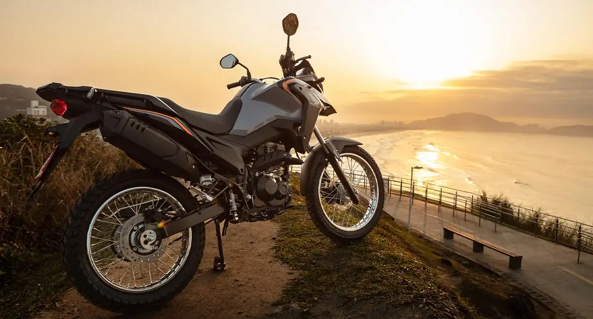 Moto XRE 190 2025 cinza em morro com areia e mar ao fundo