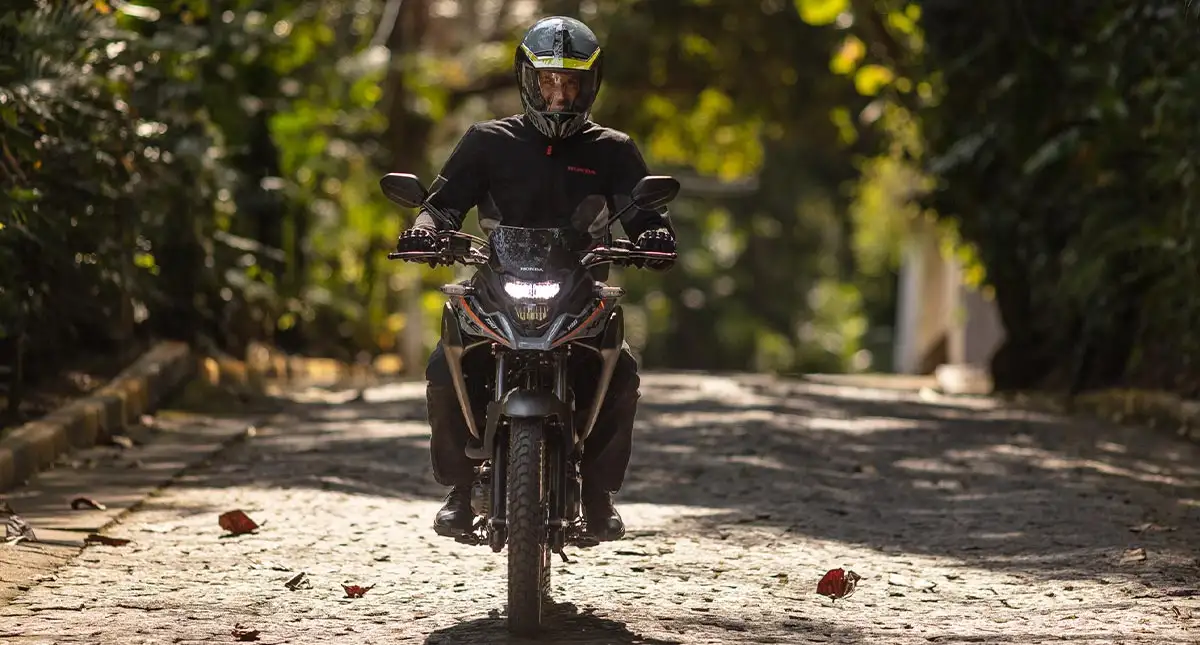 Piloto em Honda XRE 190 cinza de frente com farol aceso