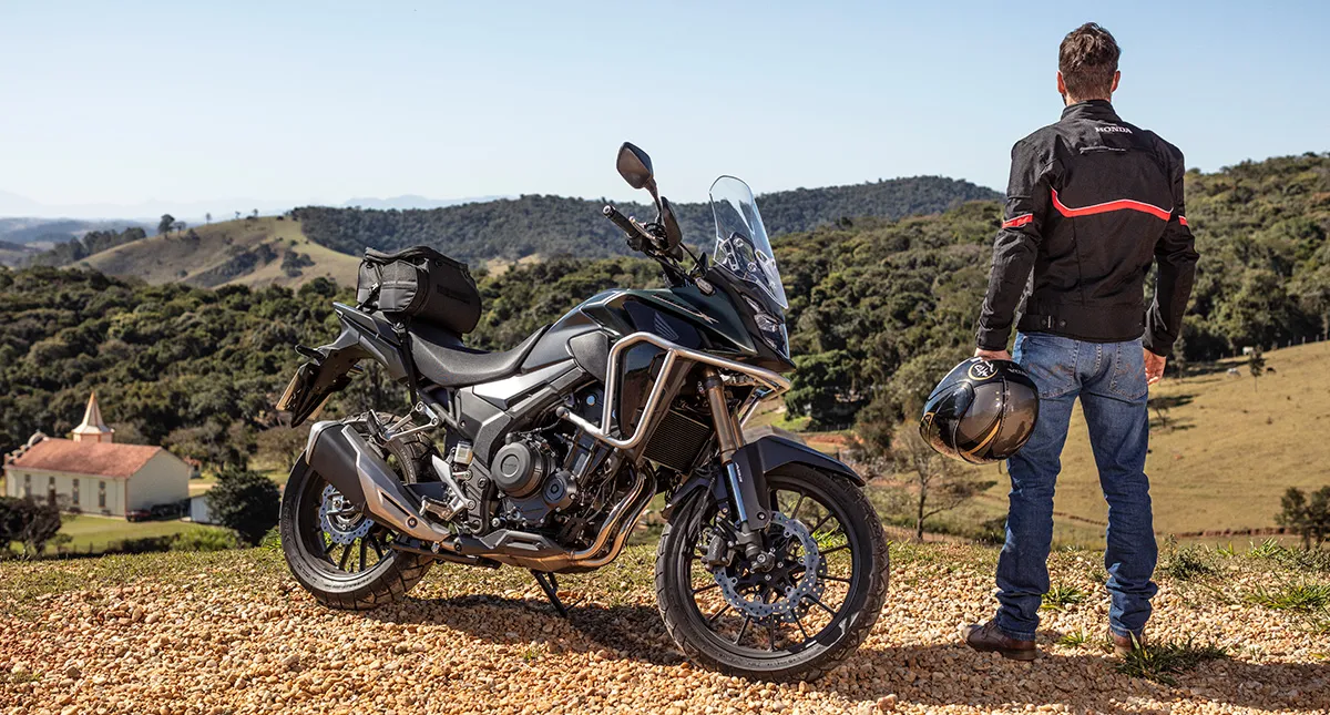 Piloto ao lado de sua motocicleta Honda CB 500X admirando paisagem