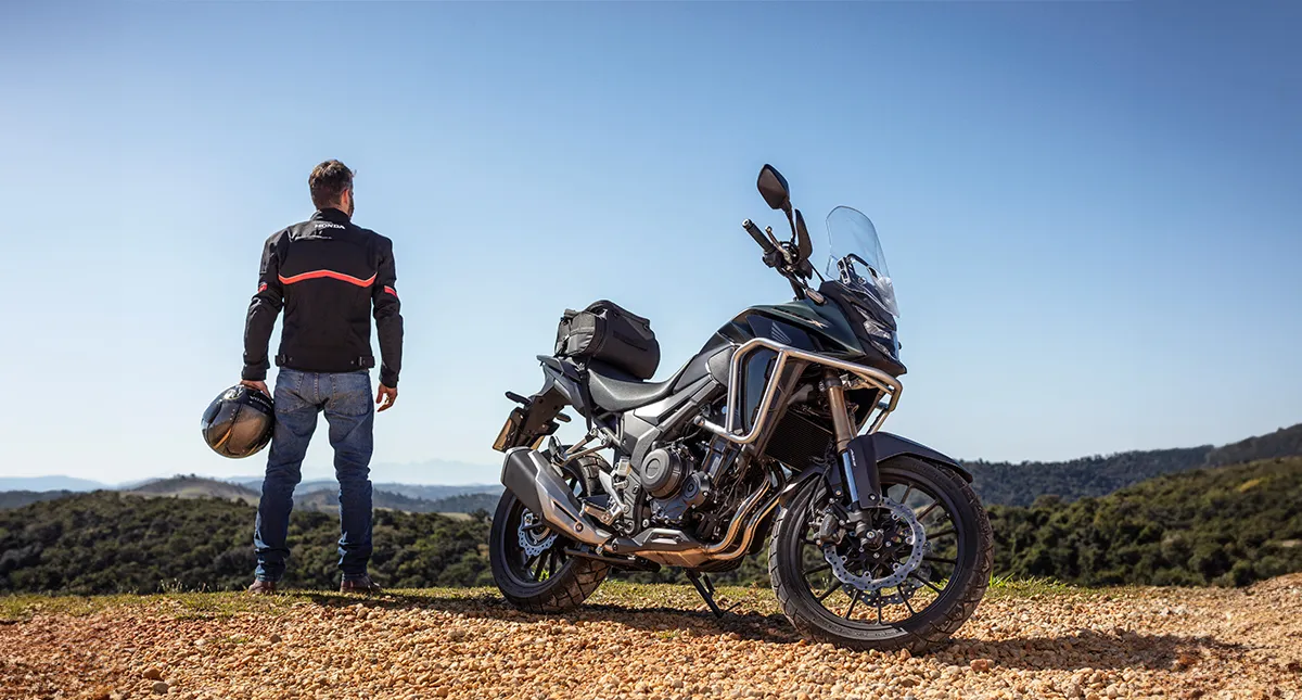Piloto ao lado de sua motocicleta Honda CB 500X admirando paisagem