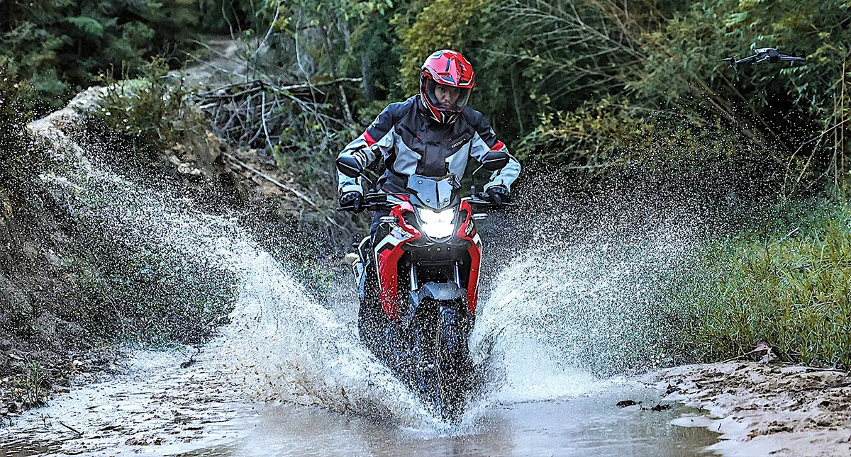 Piloto em trilha passando por poça d'água com luva para andar de motocicleta