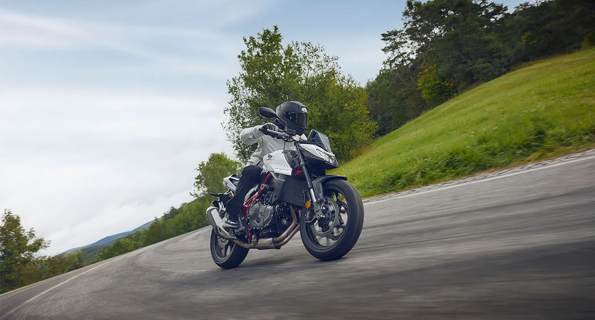 Motociclista faz curva em estrada cercada por árvores