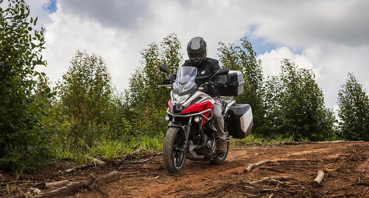 Piloto com sua Moto Honda NC 750X com malas laterais na estrada de terra