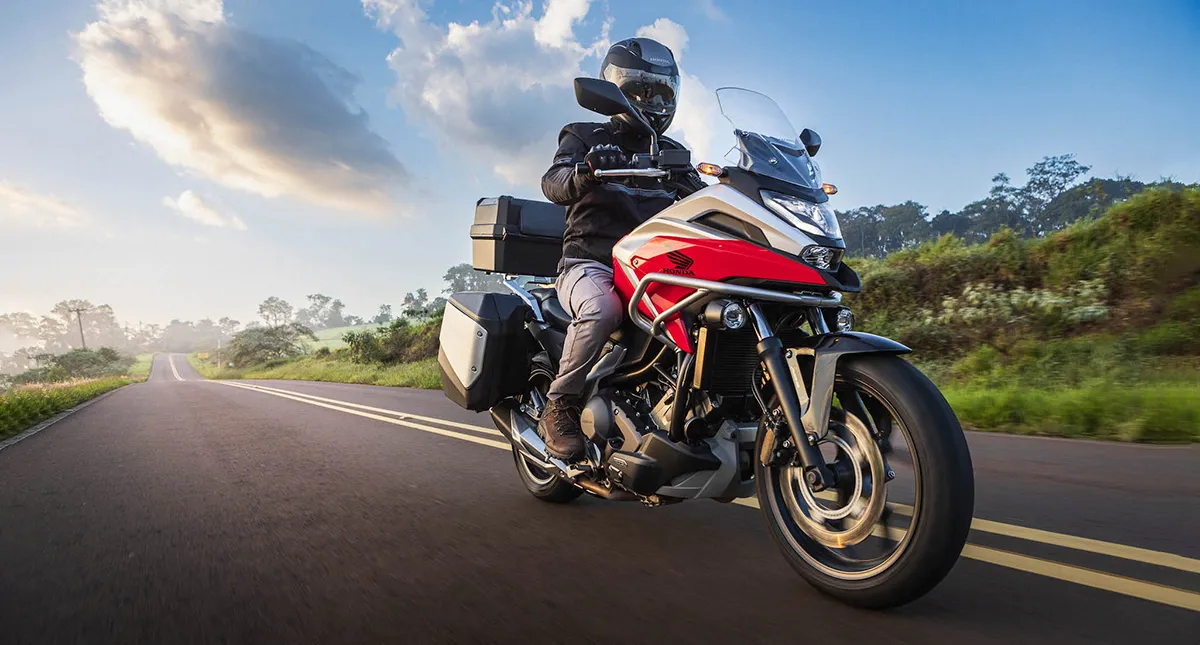 Piloto com sua Moto Honda NC 750X na estrada com paisagem ao fundo