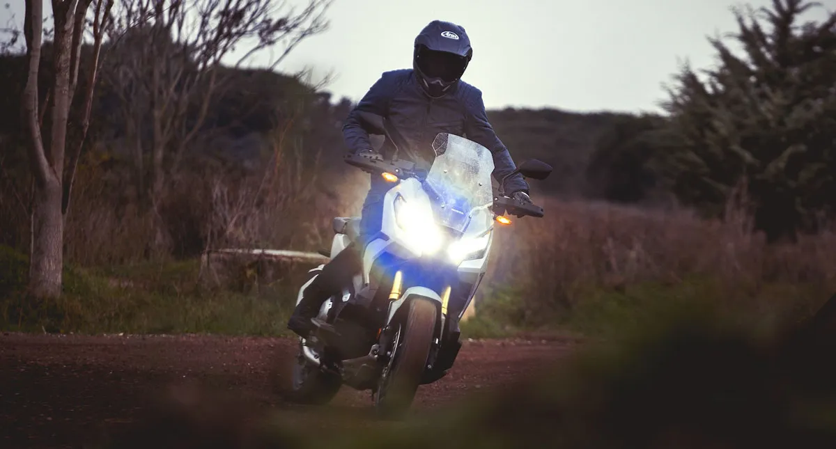 Piloto fazendo curva em estrada de terra envolta por árvores em sua Honda Scooter X-ADV Azul