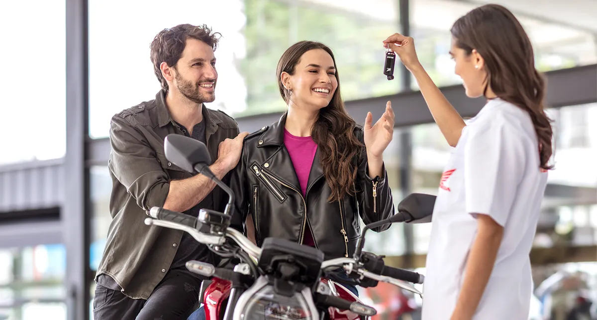 Vendedora da Concessionária Honda entregando nas mãos de um casal de homem e mulher as chaves da sua moto Honda