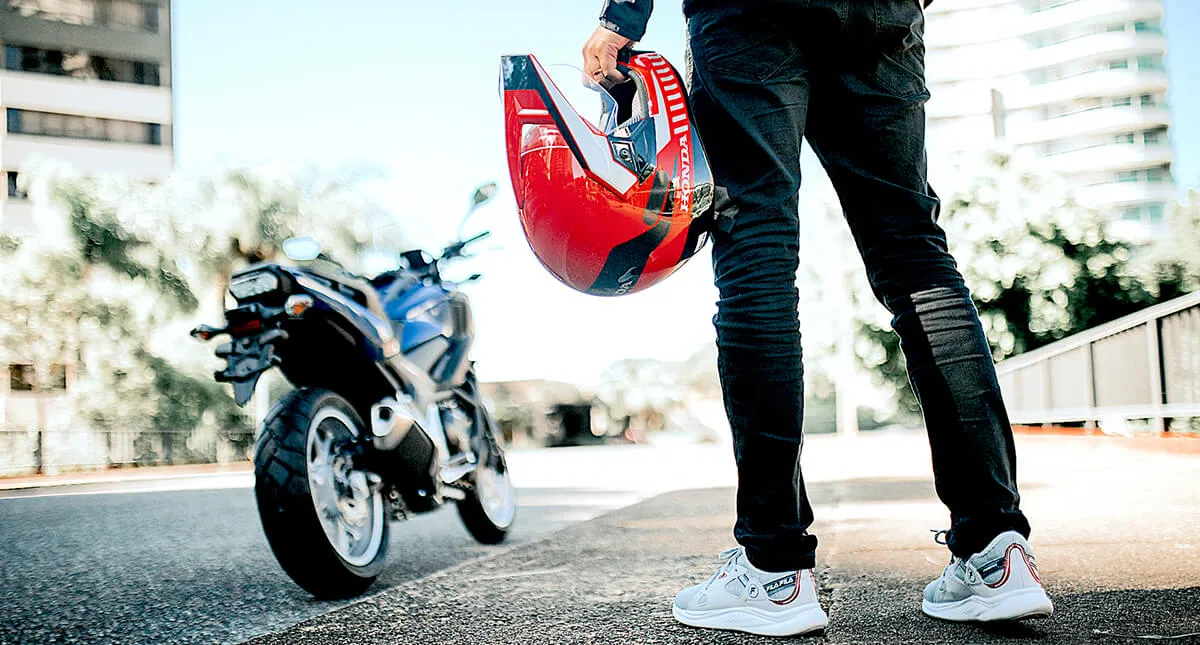 Homem a frente da moto segurando seu capacete honda vermelho