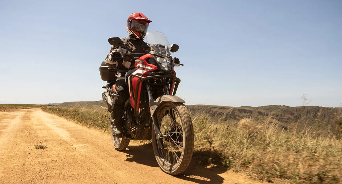 Piloto em estrada de terra com moto Honda Sahara 300 Vermelha