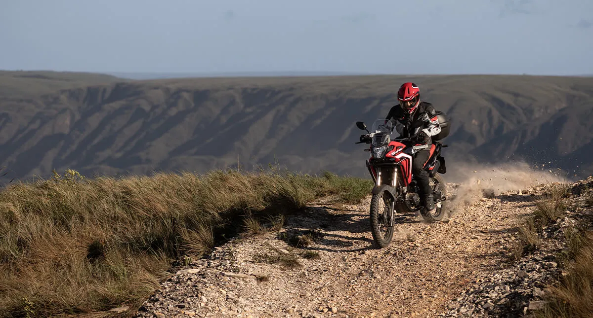 Piloto em estrada de terra com sua moto Vermelha Honda Sahara 300