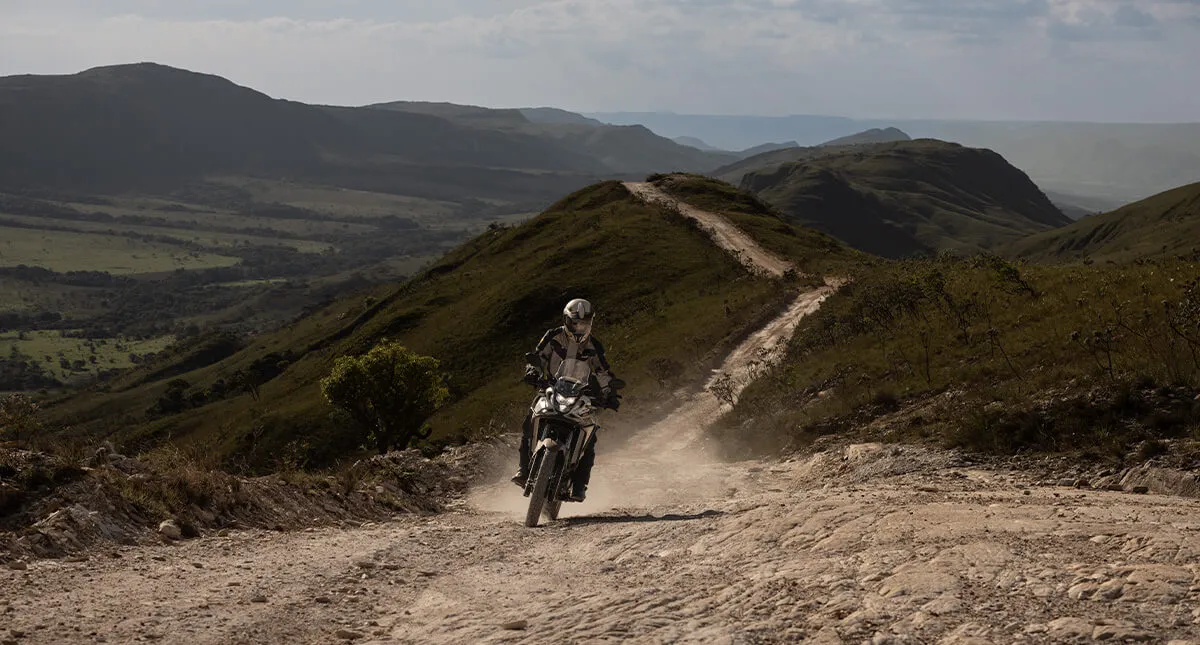 Piloto em morro com estrada de terra  em sua moto Honda Sahara 300 Prateada