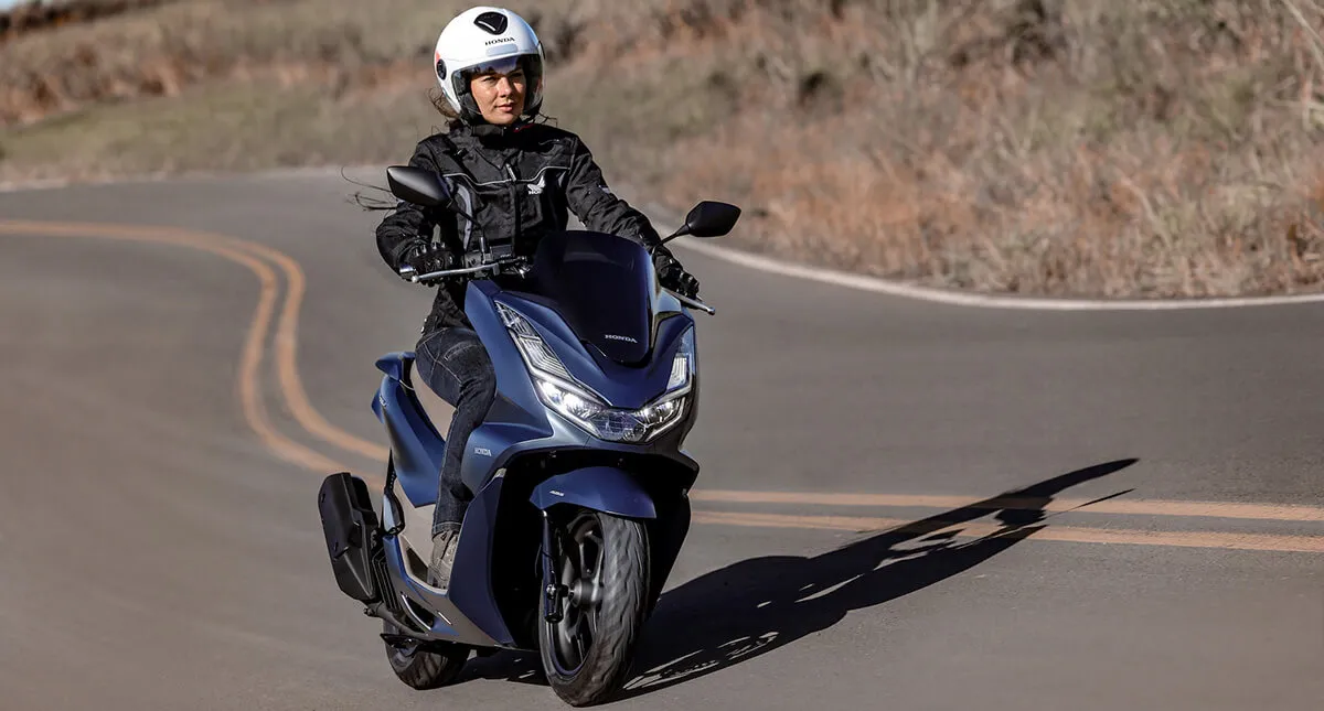 Mulher pilotando scooter PCX azul em estrada com grama ao redor