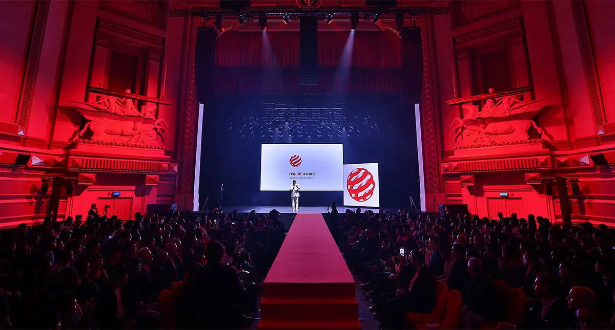Apresentador no palco do prêmio Red Dot Awards com luzes vermelhas